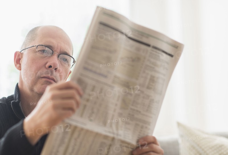 Mature man reading newspaper on sofa .