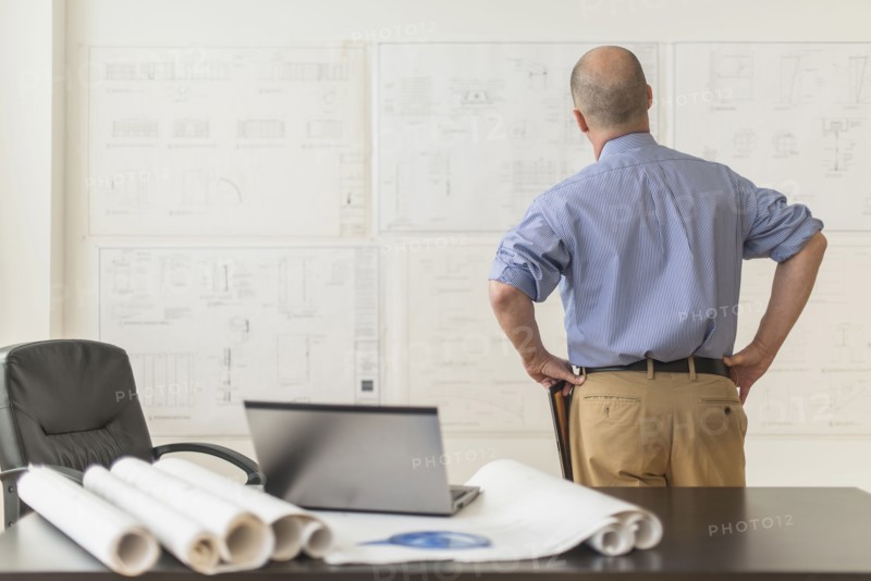 Mature architect looking at blueprints in office.