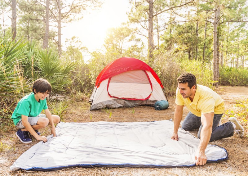 Father and son (12-13) preparing sleeping bag for camping