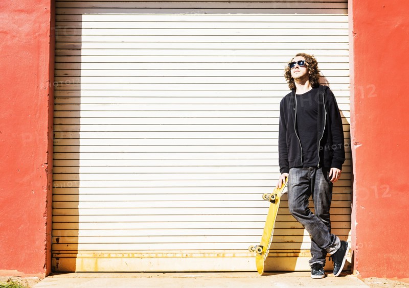 Man with skateboard leaning on garage door