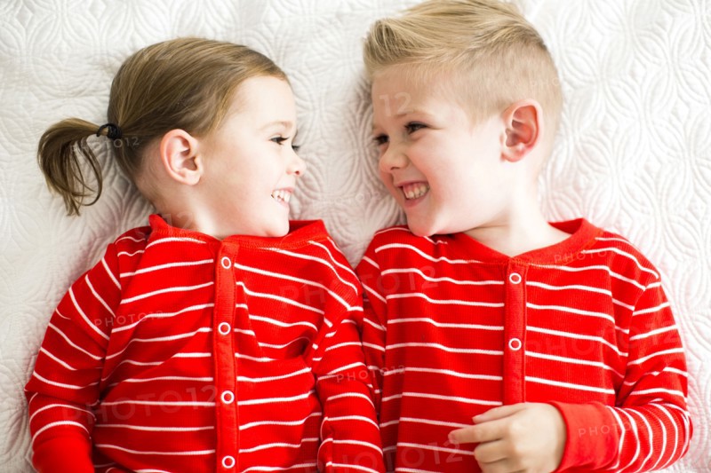 Siblings (2-3, 4-5) in red pajamas lying on bed