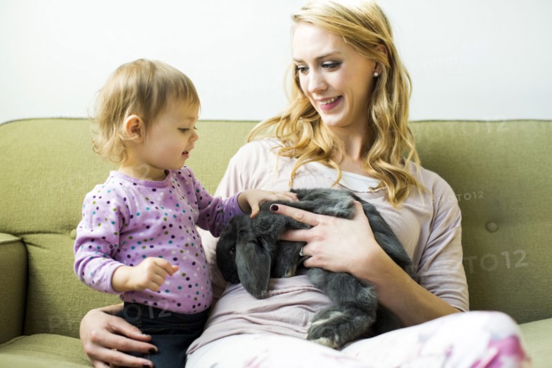 Mother and daughter (12-17 months) sitting on sofa stroking rabbit