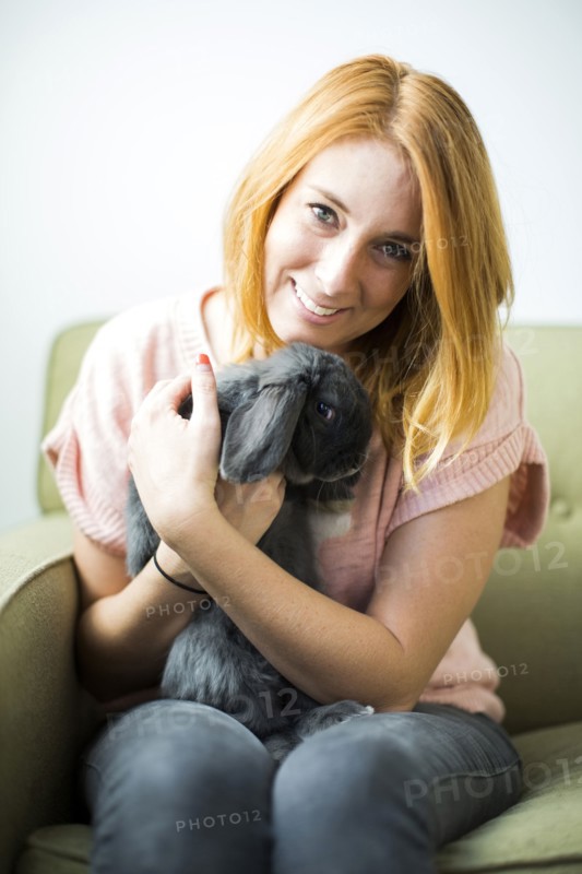 Woman sitting on sofa embracing rabbit