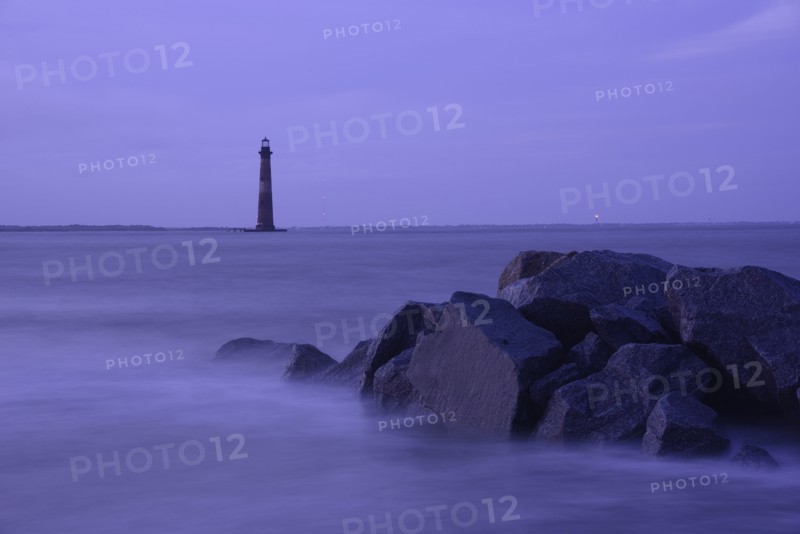 Coastal rocks and lighthouse silhouetted as dusk
