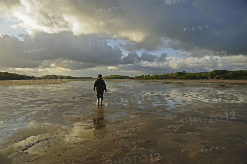 Rear view of man standing water in rubber boots, clouds in sky