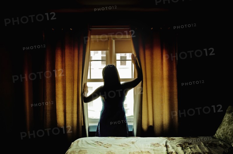 Rear view of female opening curtains at bedroom window