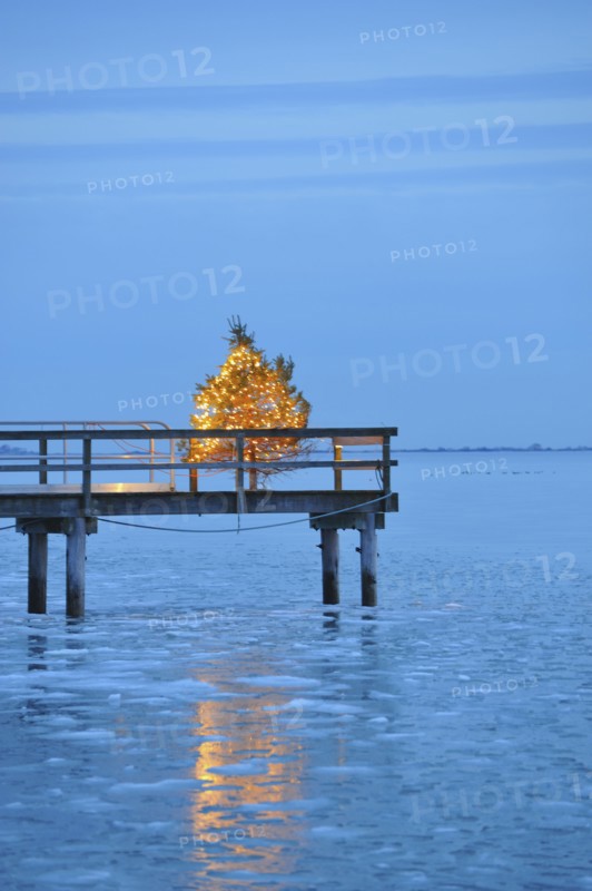 Christmas tree with yellow lights on pier, blue sky and water at dusk