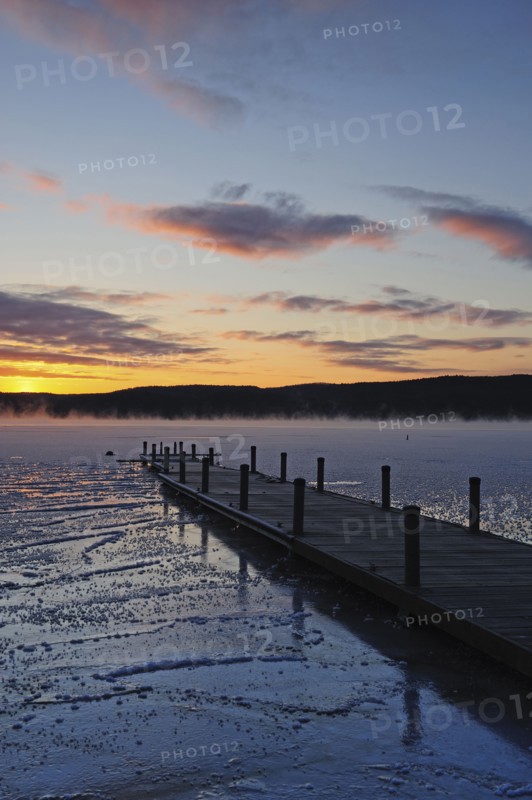 Jetty on frozen lake, hills in background at sunrise
