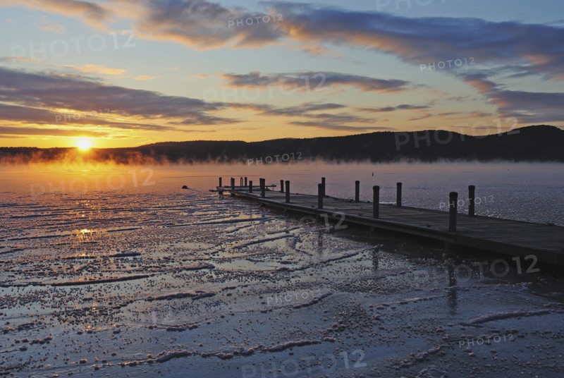 Jetty on frozen lake, hills in background at sunrise