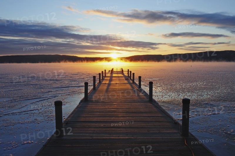 Symmetrical view of jetty on frozen lake, hills in background at sunrise