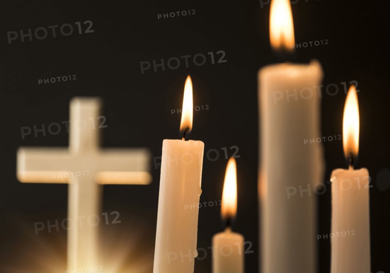 Burning candles with cross in background.