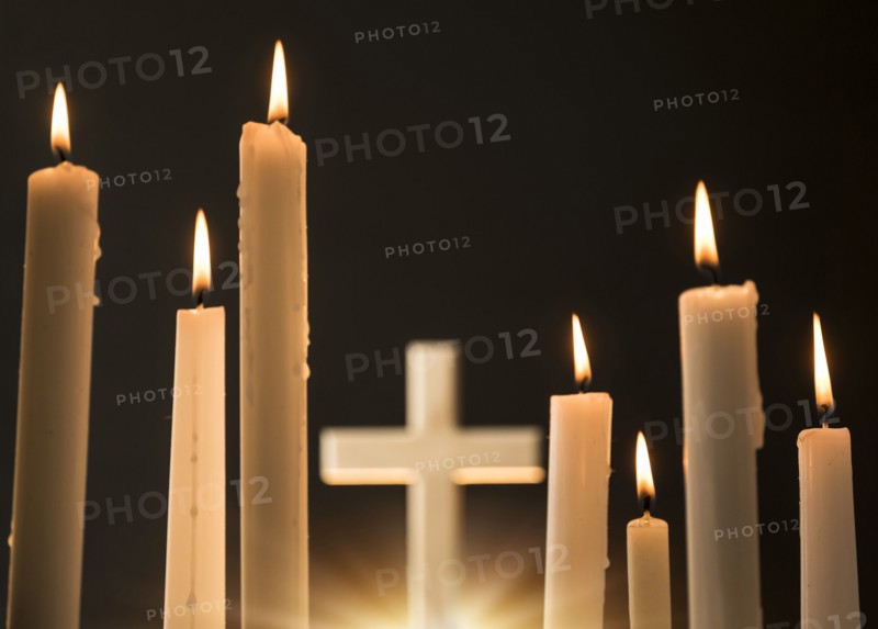 Burning candles with cross in background.