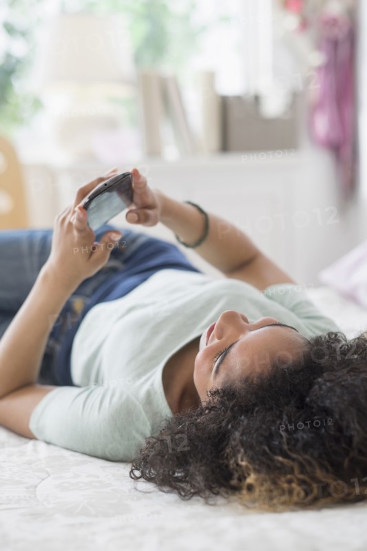 Teenage girl (16-17) texting in bedroom.