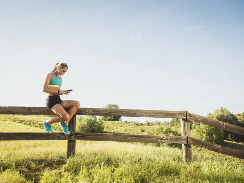 Woman sitting on fence, using smart phone