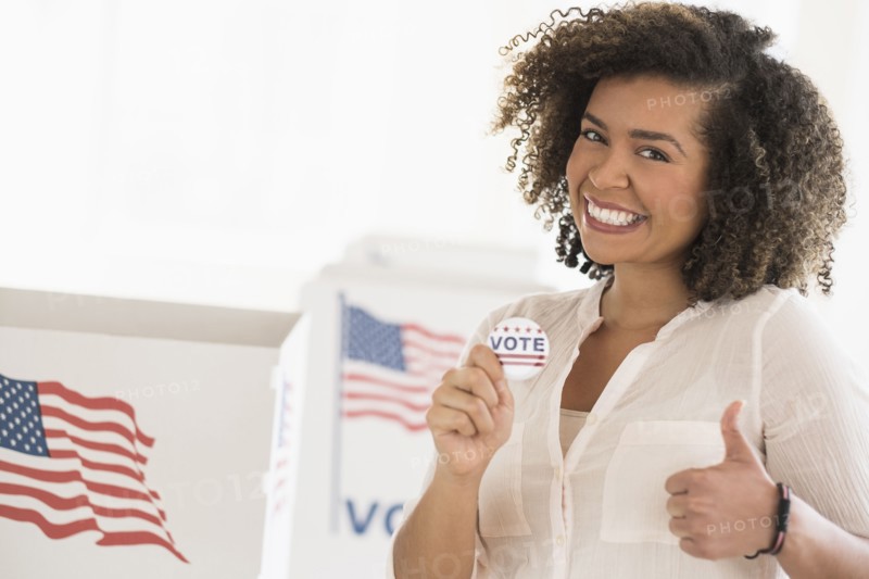 Young woman holding voting badge and smiling.