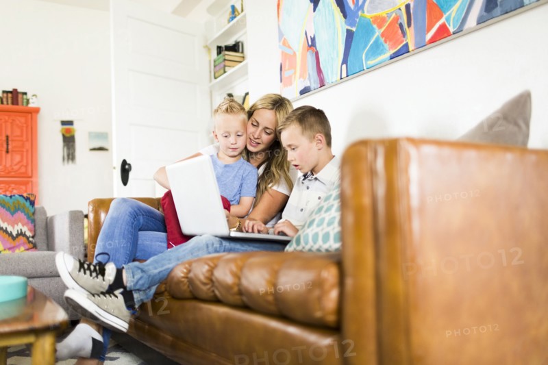 Mother with children (4-5, 6-7) using laptop on sofa