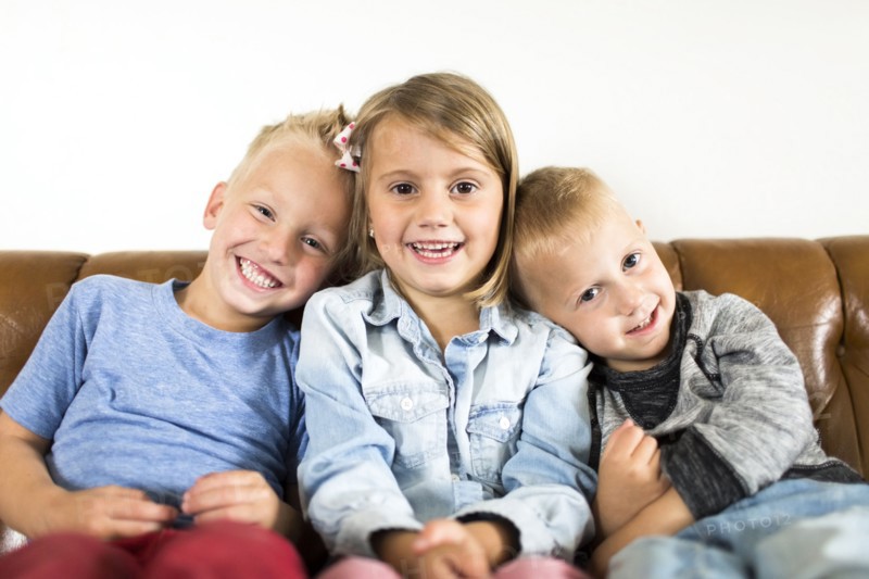 Smiling children (2-3, 4-5) sitting on sofa