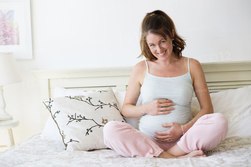 Smiling pregnant woman sitting on bed.