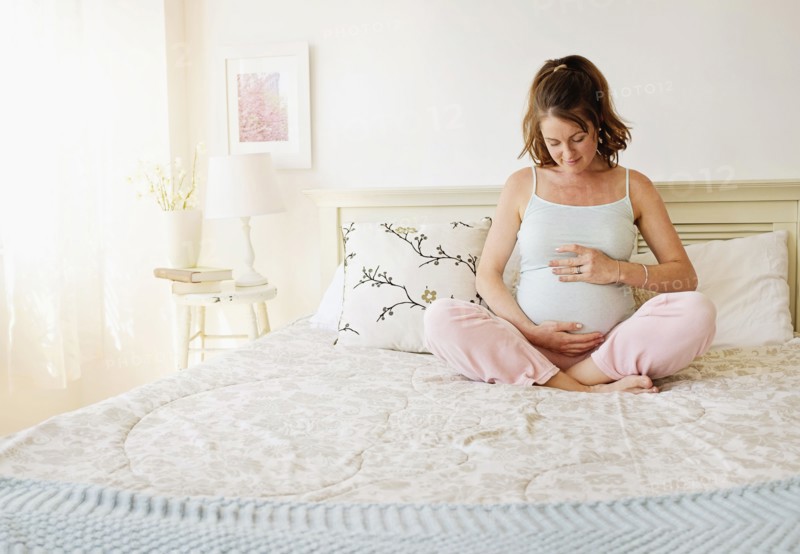 Smiling pregnant woman sitting on bed.