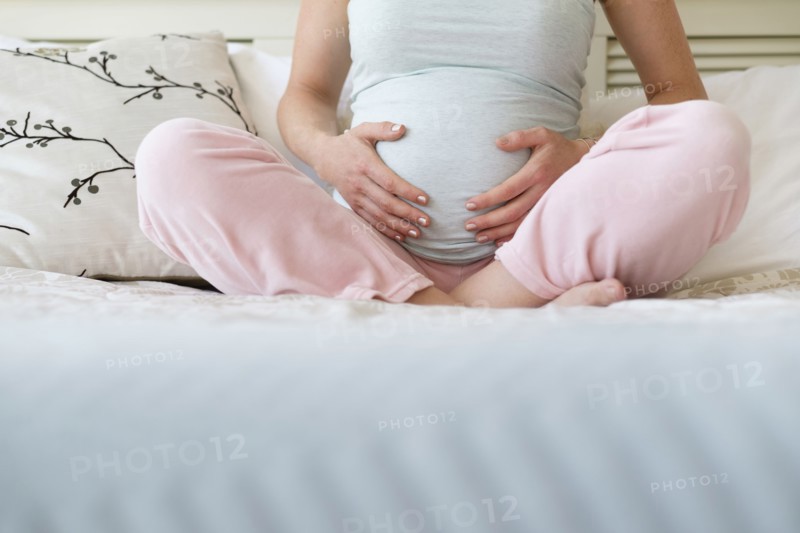 Pregnant woman sitting on bed.