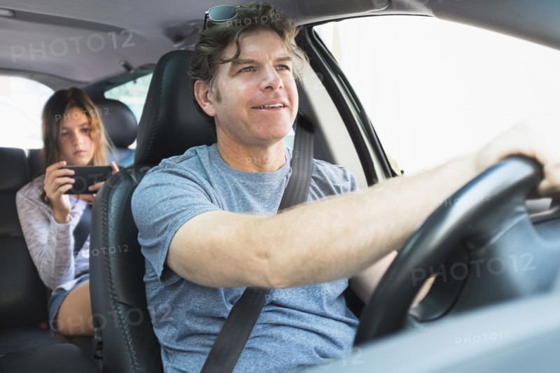 Man driving car, girl (10-11) texting in background.