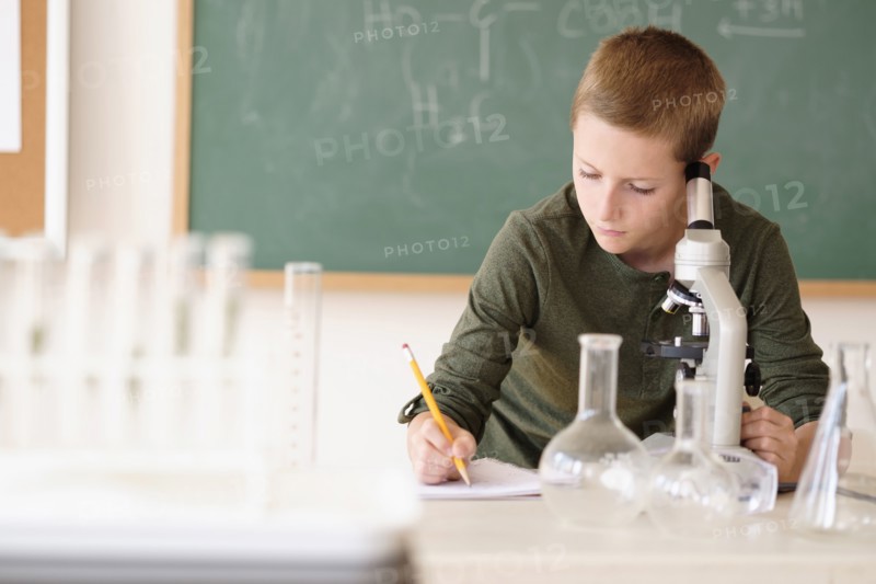 Boy (8-9) taking notes in classroom.