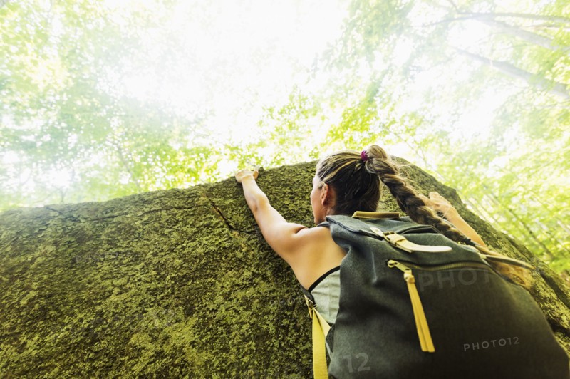 Young woman climbing on rock in forest