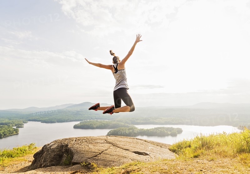 Young woman jumping over mountain top, rear view
