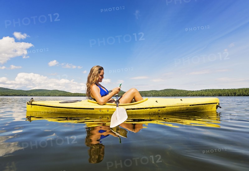 Young woman using Smartphone in kayak on lake
