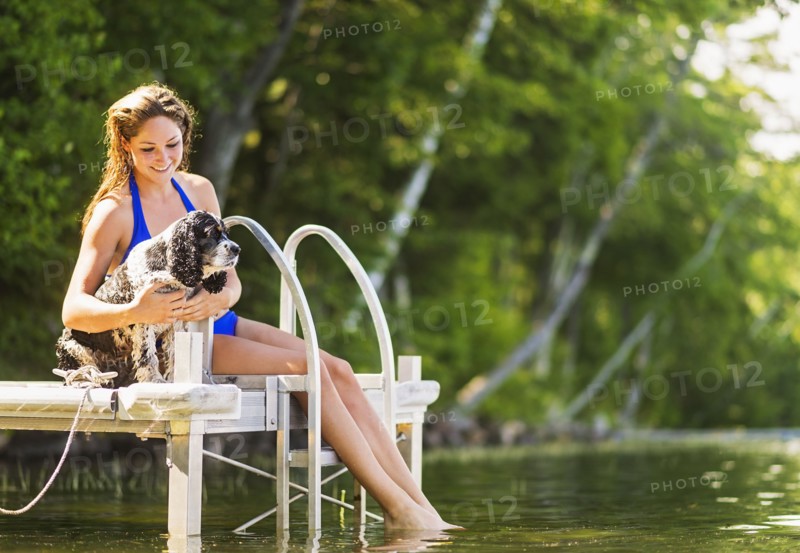 Young woman with dog sitting on jetty over lake