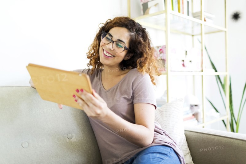 Woman sitting on sofa, using digital tablet
