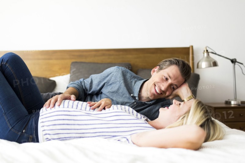 Husband lying down on bed with pregnant wife