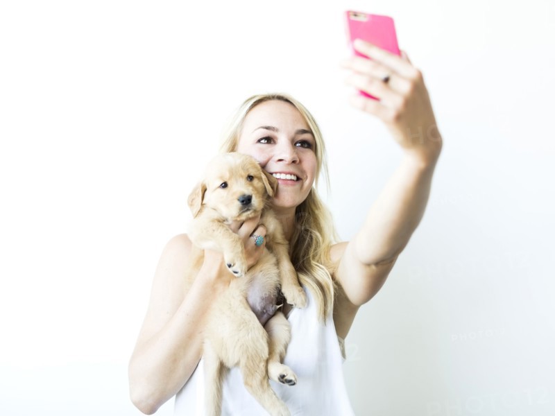 Studio shot of woman photographing self with Golden Retriever puppy