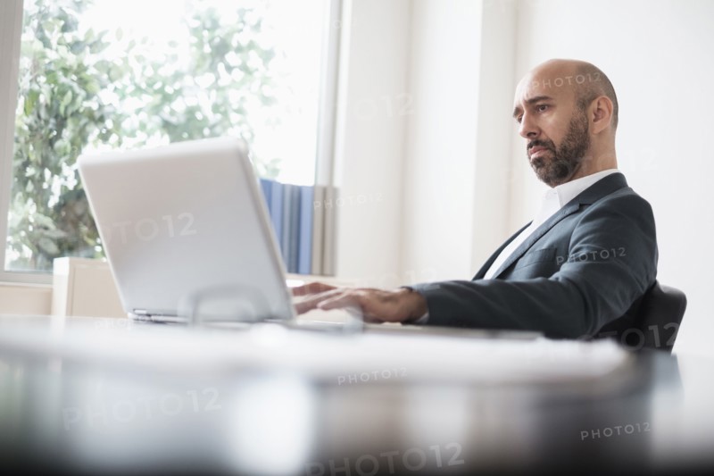 Concentrated businessman working with laptop at desk in office.