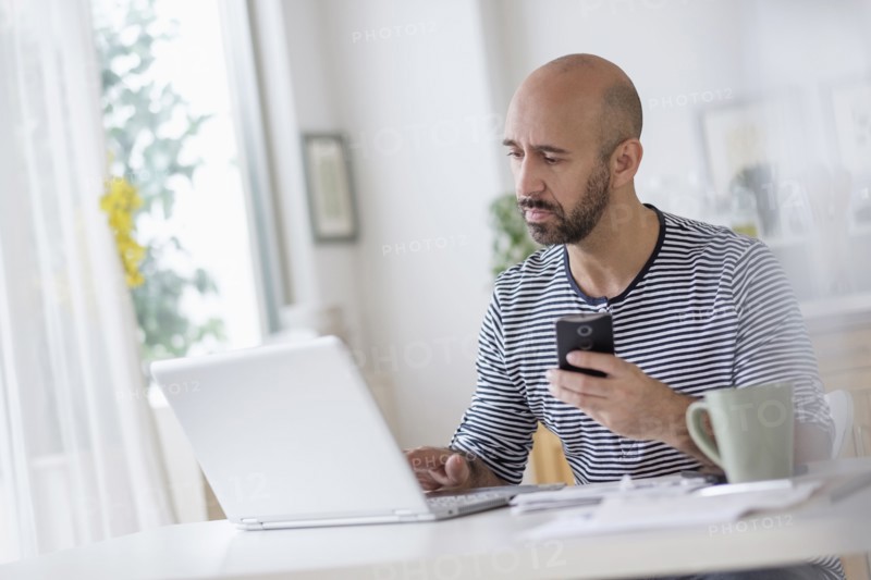 Man working with laptop and holding smart phone at table.