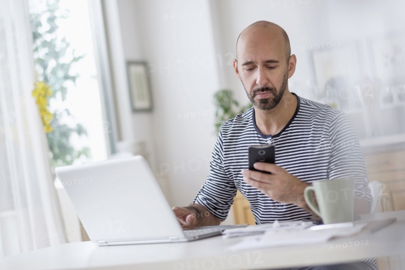 Man working with laptop and holding smart phone at table.
