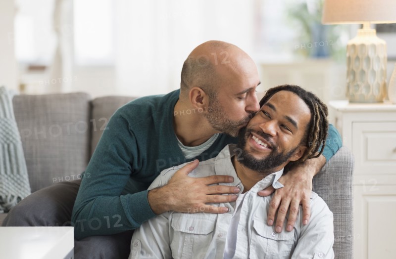 Homosexual couple kissing by sofa in living room.
