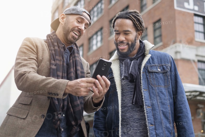 Smiley homosexual couple taking selfie with smart phone in street.