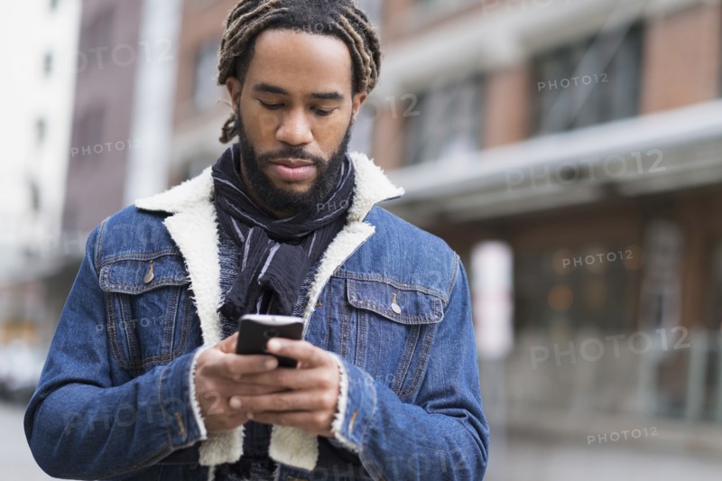 Serious man with dreadlocks using smart phone in street.