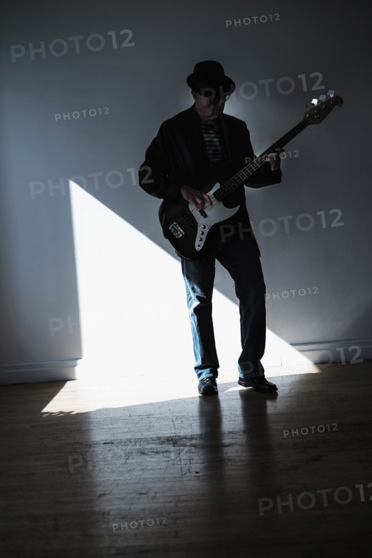 Man playing bass guitar in empty room.