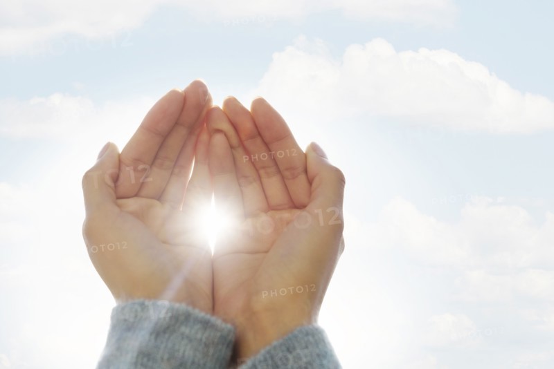 Female hands against clouds, sun shining through fingers.