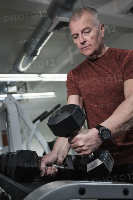 Man in health club picking up dumbbells.