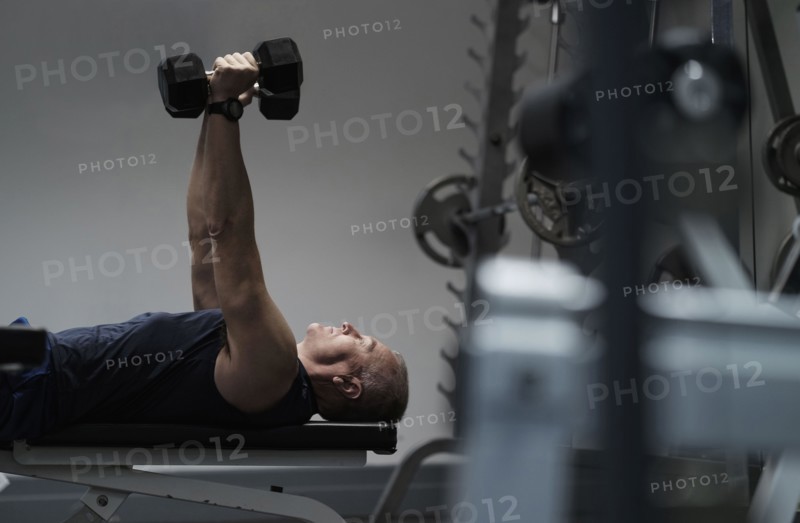 Man exercising with dumbbells on weight bench.
