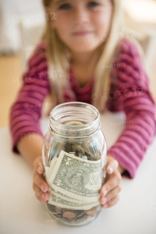 Girl (6-7) holding jar with savings