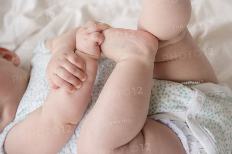 Baby girl (12-17 months) lying down with hands on feet