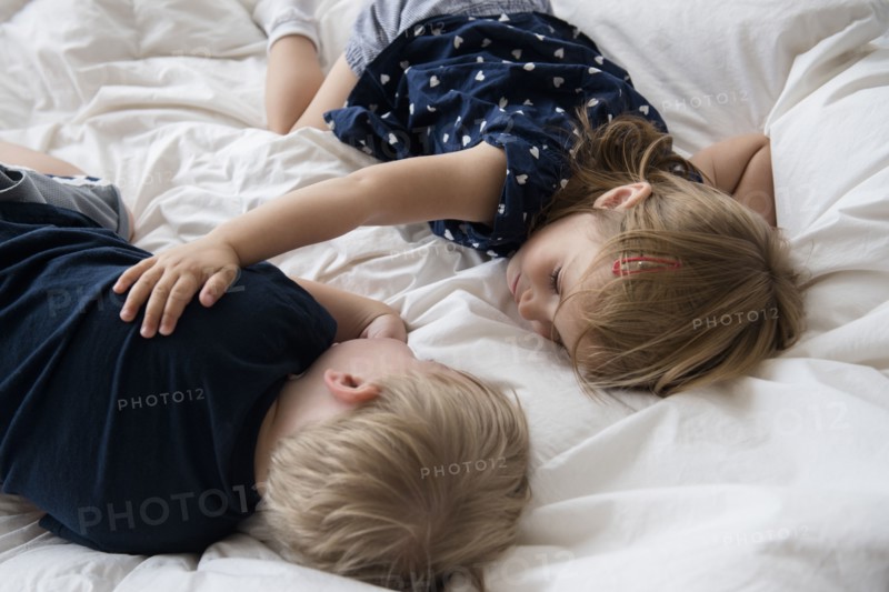 Brother (2-3) with sister (2-3) sleeping on bed