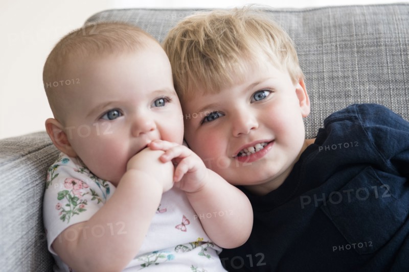 Boy (2-3) with baby sister (12-17 months) sitting on sofa