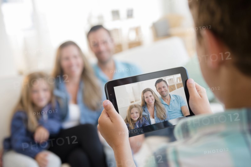 Boy (8-9) photographing family with digital tablet