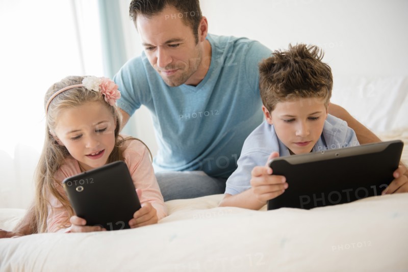 Father with son (8-9) and daughter (6-7) using tablets