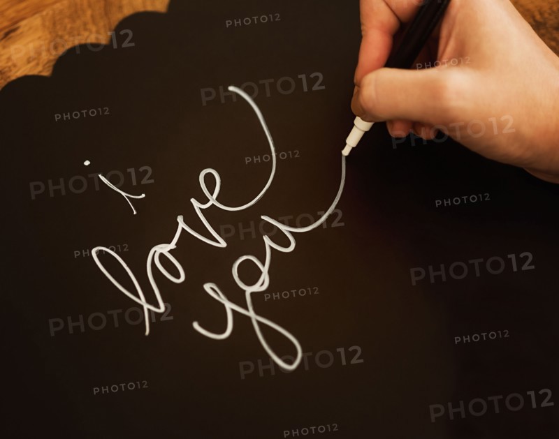 Man's hand writing I Love You on black paper